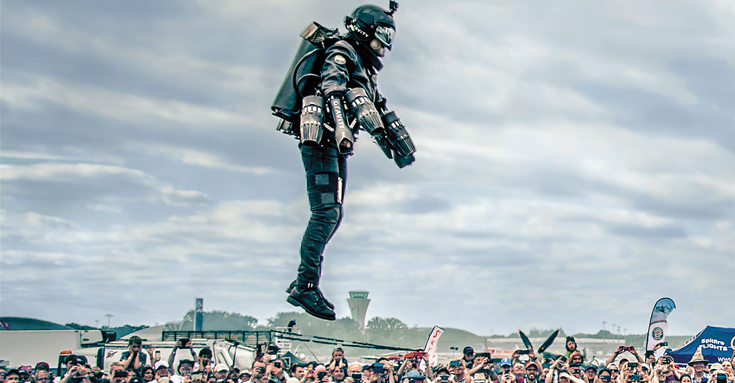 A man in a jetpack flies above a crowd.