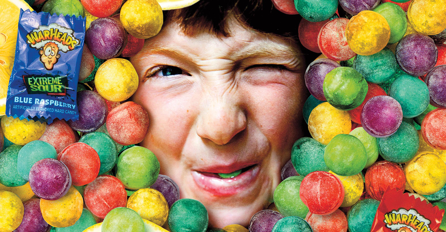 A kid puckering his lips with his face surrounded by Warheads candy.