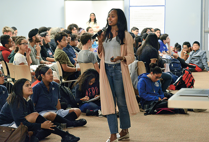 A woman speaking into a microphone in front of a large group of teenagers