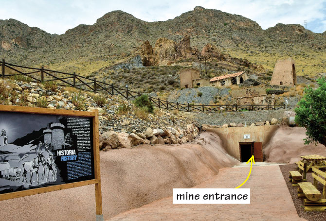A red rock entrance carved into a a green, scrub-covered hillside