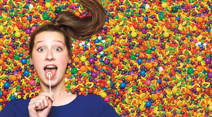 A teenager with a lollipop laying on top of colorful candy