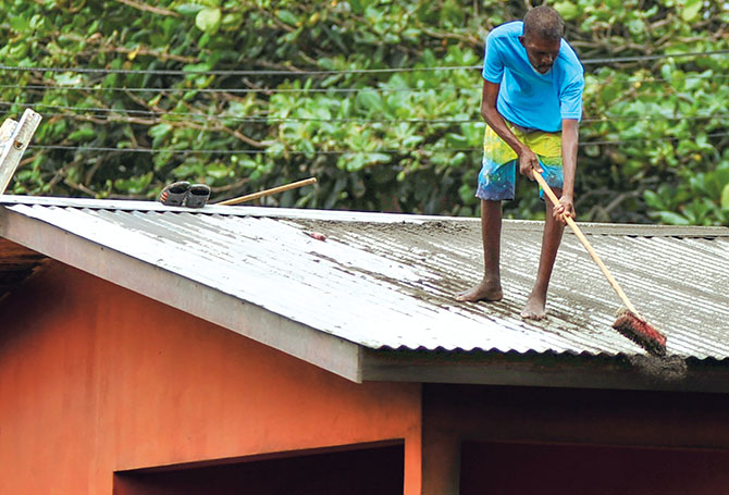 Person standing on a roof and sweeping off ash